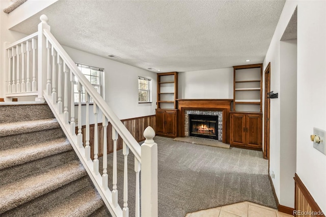 stairway with carpet flooring, a textured ceiling, and a glass covered fireplace
