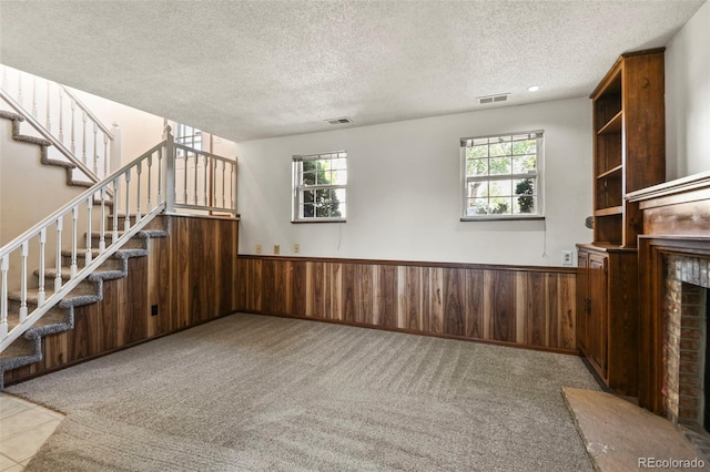unfurnished living room with a wainscoted wall, plenty of natural light, a textured ceiling, stairway, and wood walls
