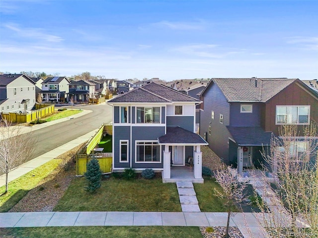 traditional home with a residential view, covered porch, roof with shingles, and a front lawn