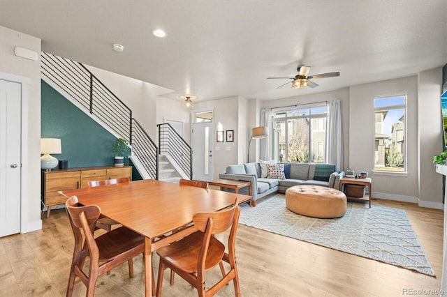 dining space with stairs, light wood-style floors, baseboards, and ceiling fan