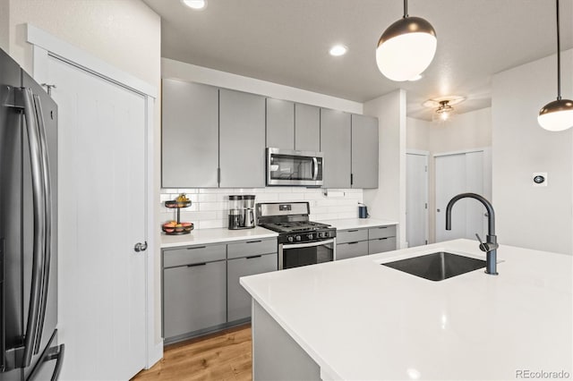 kitchen featuring tasteful backsplash, gray cabinetry, stainless steel appliances, and a sink