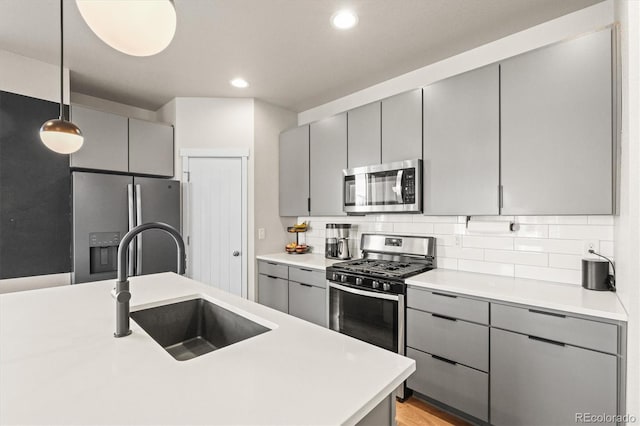 kitchen with gray cabinetry, a sink, appliances with stainless steel finishes, light countertops, and decorative backsplash