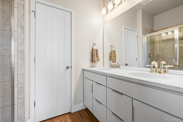 bathroom with double vanity, wood finished floors, a stall shower, and a sink