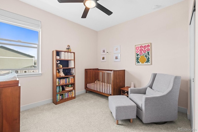 carpeted bedroom with baseboards, a nursery area, and ceiling fan