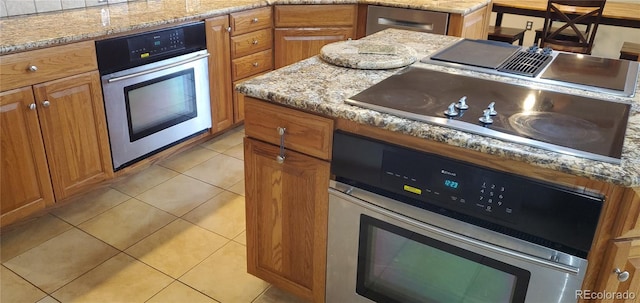 kitchen with light stone counters, oven, light tile patterned flooring, and black electric cooktop