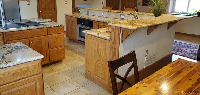 8120 S Jay Dr, Littleton, CO 80128 - kitchen featuring stainless steel oven, black electric stovetop, a kitchen breakfast bar, light tile patterned floors, and light stone counters