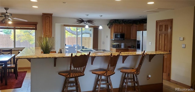 kitchen featuring appliances with stainless steel finishes, light tile patterned flooring, a kitchen breakfast bar, ceiling fan, and light stone counters