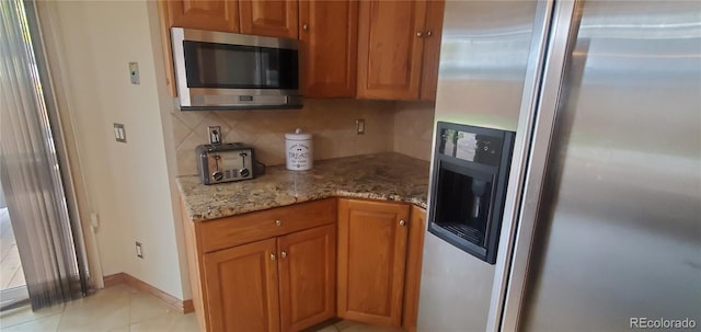 kitchen with light stone countertops, appliances with stainless steel finishes, backsplash, and light tile patterned floors