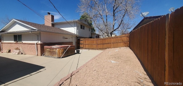 8120 S Jay Dr, Littleton, CO 80128 - view of home's exterior with a hot tub, a fenced backyard, a patio, a chimney, and brick siding