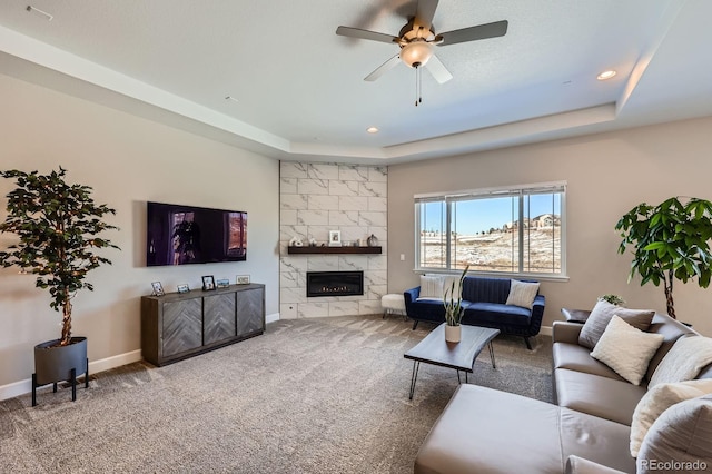 carpeted living area with a ceiling fan, a tray ceiling, baseboards, and a premium fireplace