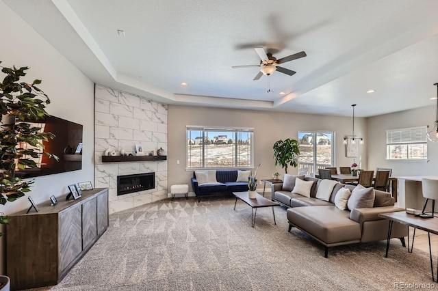 carpeted living area featuring ceiling fan, a tiled fireplace, a raised ceiling, and recessed lighting