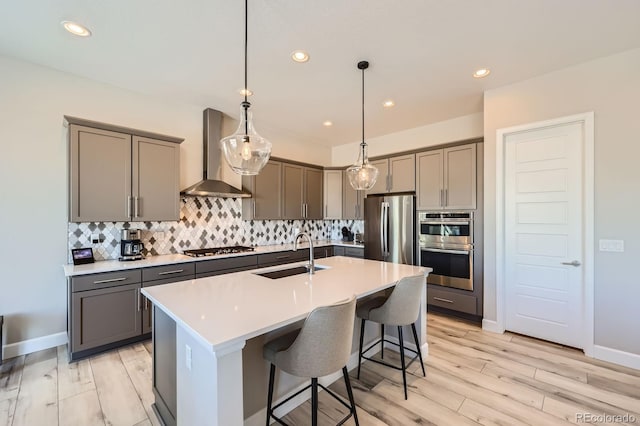 kitchen featuring stainless steel appliances, gray cabinets, a sink, and wall chimney exhaust hood