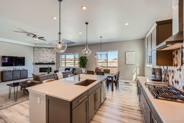 kitchen featuring dishwasher, wall chimney exhaust hood, a fireplace, gas cooktop, and a sink