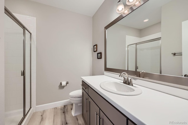 full bath with toilet, vanity, a shower stall, wood finished floors, and baseboards