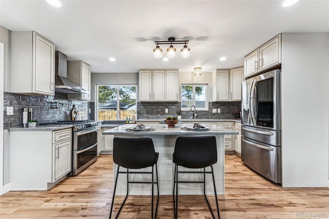 kitchen featuring a breakfast bar area, stainless steel appliances, a sink, wall chimney range hood, and a center island