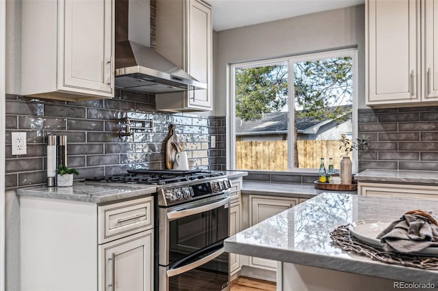 kitchen featuring range with two ovens, backsplash, stone countertops, light wood-style floors, and wall chimney range hood