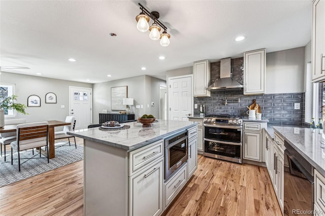 kitchen featuring tasteful backsplash, wall chimney range hood, light stone countertops, light wood-type flooring, and double oven range