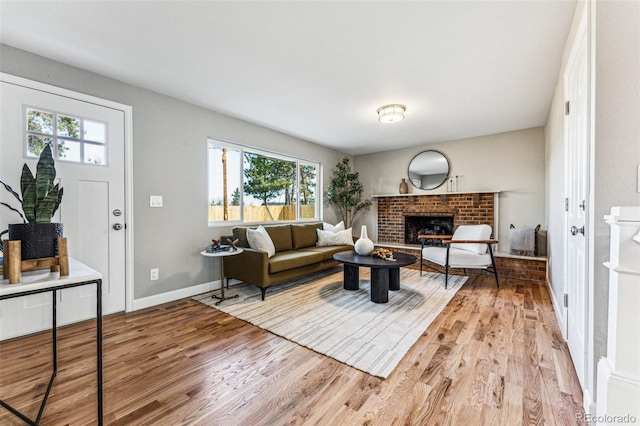 living room with a brick fireplace, light wood-style flooring, and baseboards