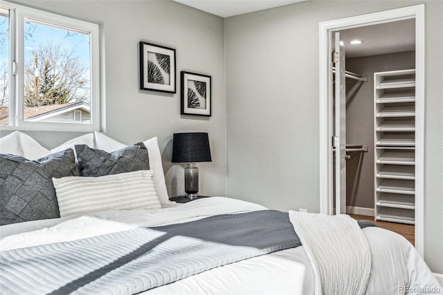 bedroom with baseboards, a walk in closet, and wood finished floors