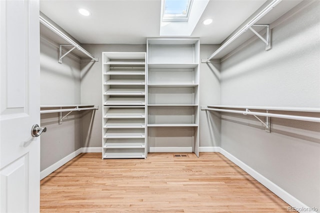 spacious closet with light wood finished floors and a skylight