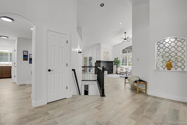 hall with an upstairs landing, light wood finished floors, arched walkways, baseboards, and high vaulted ceiling