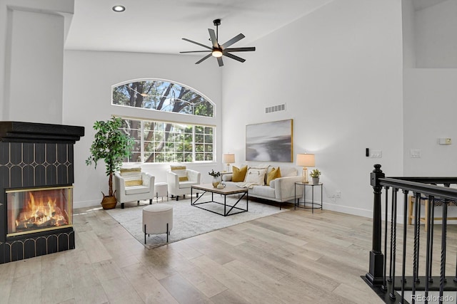 living room featuring a glass covered fireplace, wood finished floors, high vaulted ceiling, ceiling fan, and baseboards