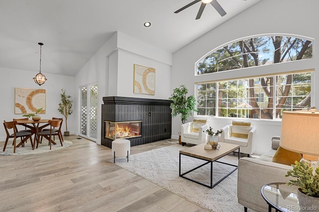 living area featuring high vaulted ceiling, a ceiling fan, wood finished floors, a glass covered fireplace, and baseboards
