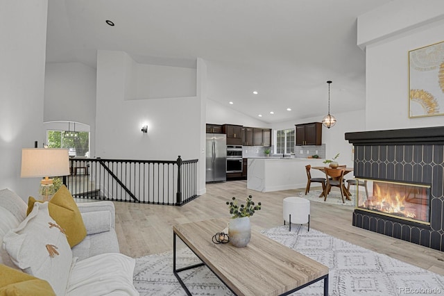 living area with light wood-style floors, plenty of natural light, recessed lighting, high vaulted ceiling, and a multi sided fireplace