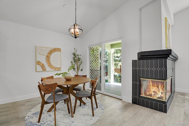 dining area with a glass covered fireplace, wood finished floors, baseboards, a chandelier, and high vaulted ceiling