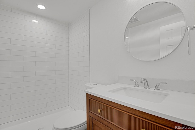 bathroom featuring toilet, vanity, a tile shower, and recessed lighting