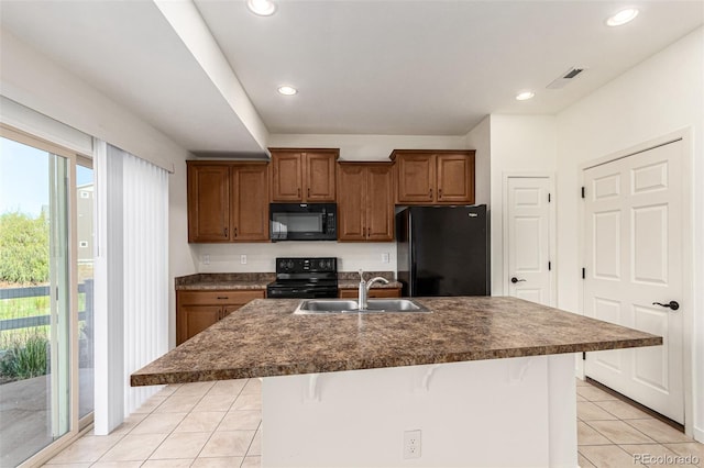 kitchen with light tile patterned floors, sink, black appliances, a kitchen breakfast bar, and a kitchen island with sink