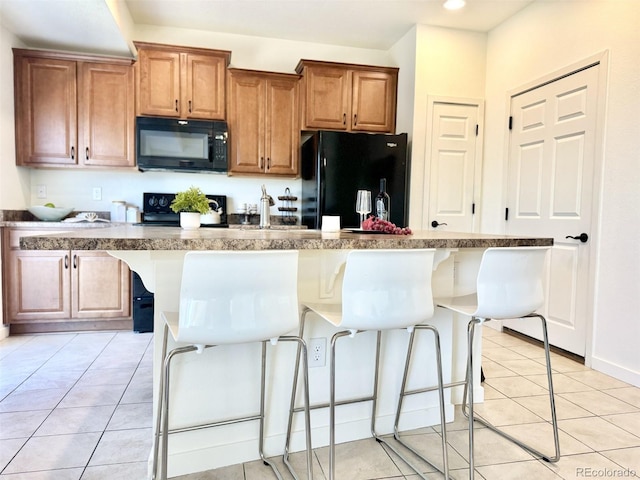 kitchen featuring a breakfast bar, light tile patterned flooring, a center island with sink, and black appliances