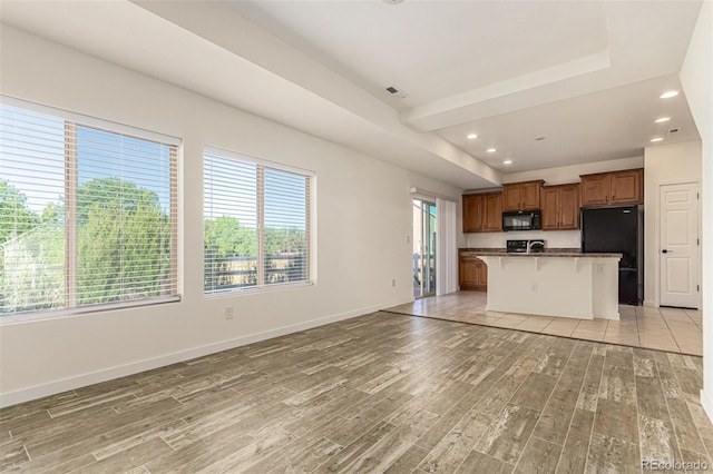 kitchen featuring light wood-style flooring, baseboards, open floor plan, black appliances, and brown cabinetry