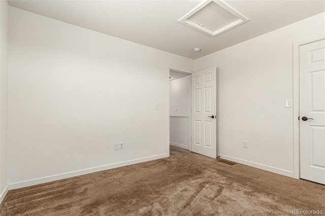 carpeted empty room with attic access, visible vents, and baseboards