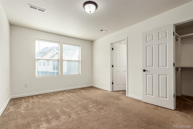 unfurnished bedroom featuring a walk in closet, carpet, visible vents, a textured ceiling, and baseboards