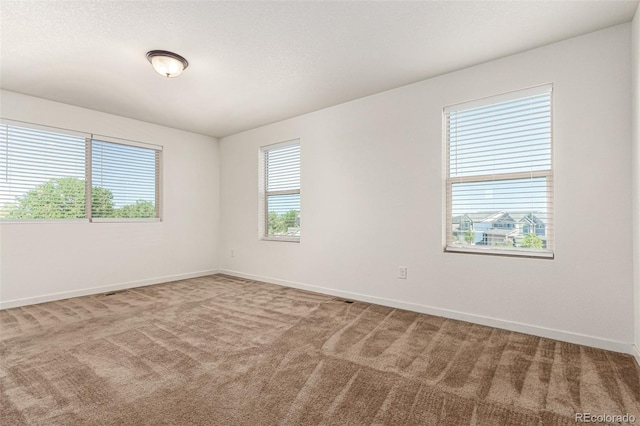 carpeted spare room with visible vents, baseboards, and a textured ceiling