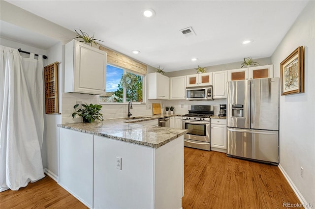 kitchen with light hardwood / wood-style flooring, appliances with stainless steel finishes, kitchen peninsula, decorative backsplash, and white cabinets