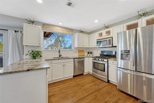 kitchen featuring stainless steel appliances, white cabinetry, sink, and light stone counters