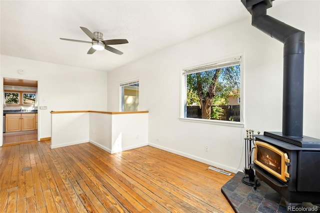 unfurnished living room featuring sink, light wood-type flooring, ceiling fan, and a wood stove