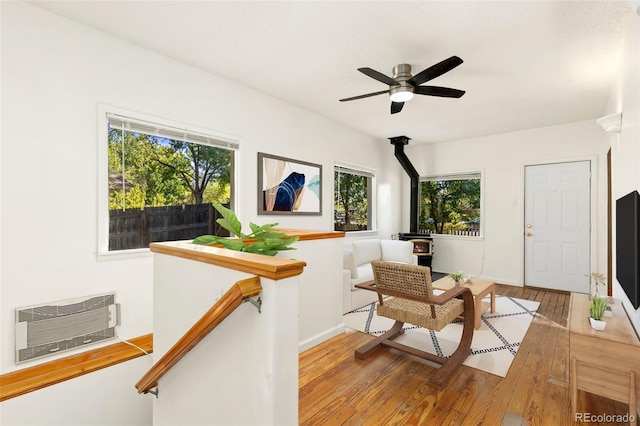 sitting room with ceiling fan, hardwood / wood-style flooring, a wall mounted AC, and a wood stove