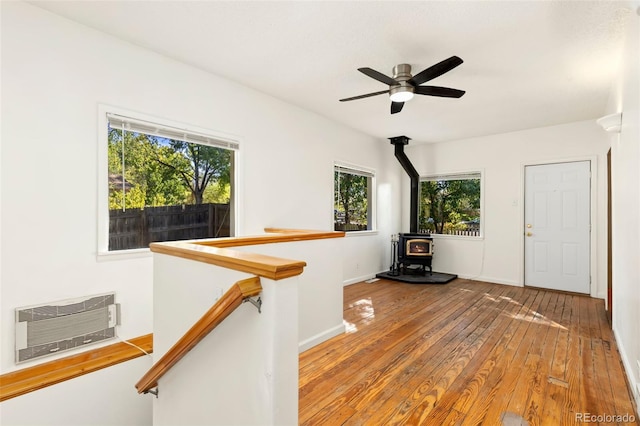 interior space featuring hardwood / wood-style flooring, a wood stove, a wall mounted air conditioner, and ceiling fan