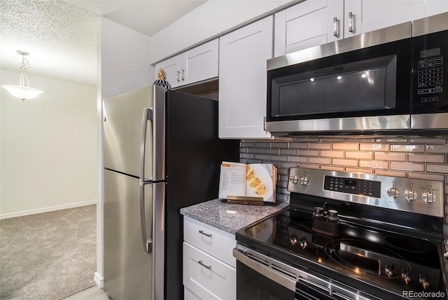 kitchen featuring light carpet, appliances with stainless steel finishes, pendant lighting, decorative backsplash, and white cabinetry