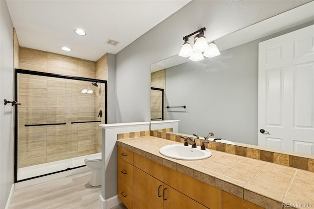 bathroom with a shower stall, toilet, wood finished floors, vanity, and recessed lighting