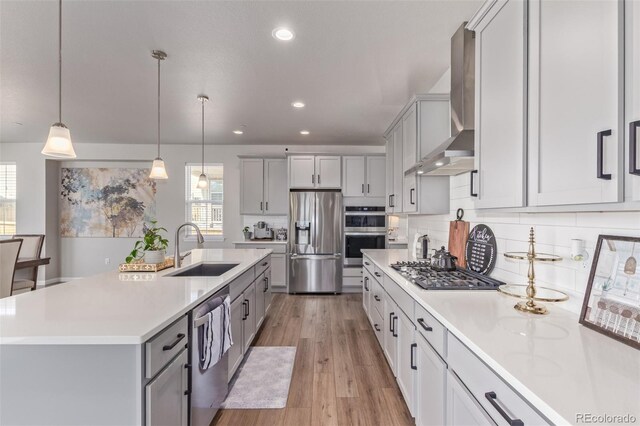 kitchen with stainless steel appliances, wall chimney range hood, a sink, gray cabinets, and healthy amount of natural light