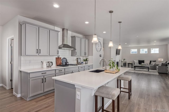 kitchen featuring gray cabinetry, wall chimney range hood, a sink, a breakfast bar area, and recessed lighting