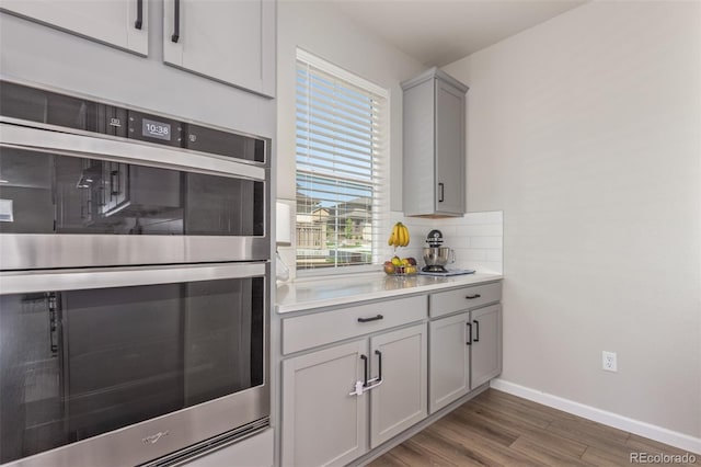 kitchen featuring gray cabinetry, wood finished floors, baseboards, light countertops, and backsplash