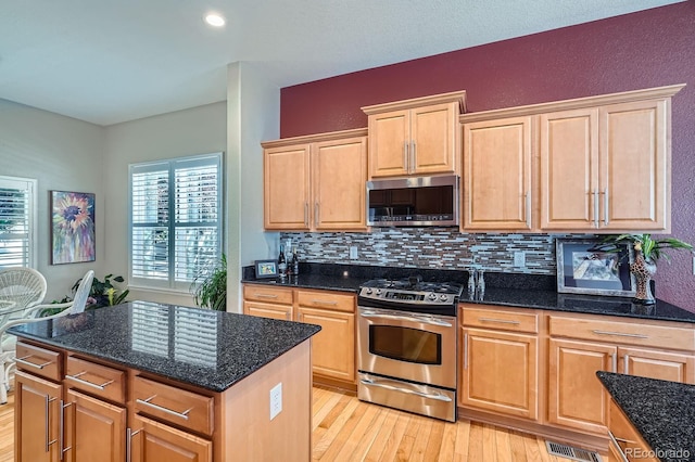 16644 Eolus Way, Broomfield, CO 80023 - kitchen with appliances with stainless steel finishes, decorative backsplash, light wood-type flooring, dark stone counters, and a kitchen island