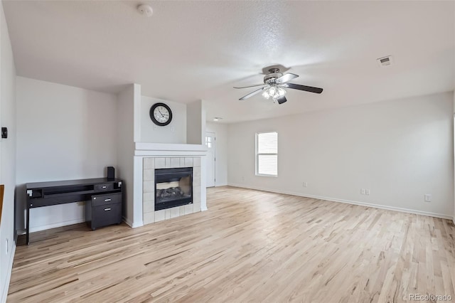 unfurnished living room with a tiled fireplace, light hardwood / wood-style flooring, a textured ceiling, and ceiling fan