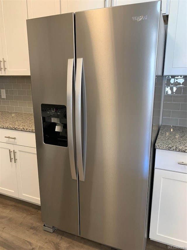 kitchen featuring dark wood-type flooring, white cabinetry, tasteful backsplash, stainless steel fridge, and light stone countertops