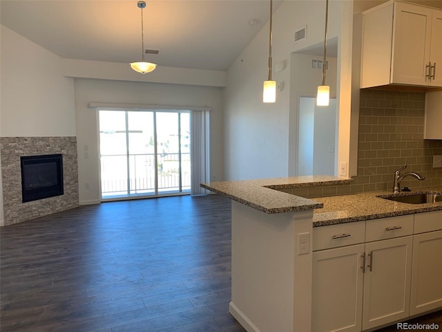 kitchen with sink, white cabinetry, hanging light fixtures, light stone counters, and vaulted ceiling